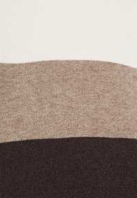 Gros plan d’un tissu tricoté avec des blocs de couleur horizontaux en crème, marron clair et marron foncé.