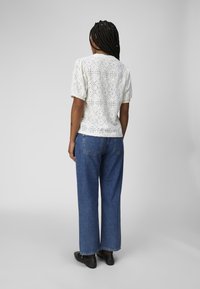Witte oogjesblouse met korte pofmouwen, voorzien van bloemen uitsparingen, gecombineerd met hoogwaisted blauwe denim jeans en zwarte schoenen.
