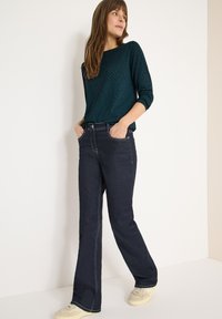 Tmavě modré rozšířené džíny s světlými švy a volným střihem, doplněné o tyrkysový vzorovaný top s ¾ rukávy.