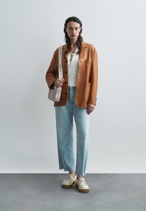 Brown faux leather blazer over white knit top, blue wide-leg jeans with frayed hem, and chunky beige shoes with floral accents.