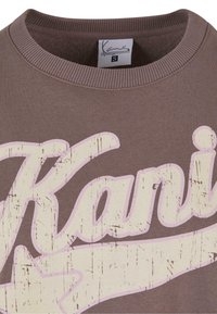 Felpa marrone con una grande stampa consumata in rosa della parola "Kani" con una stella accentata, colletto tondo e polsini a coste. Etichetta di taglia S visibile.