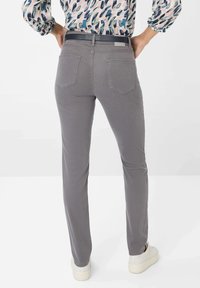 Pantaloni grigi slim fit con tasche posteriori, abbinati a una blouse a fantasia. I pantaloni hanno una texture liscia e sono abbinati a sneakers bianche.