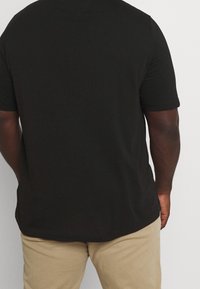Černé bavlněné tričko s krátkými rukávy, kulatým výstřihem a volným střihem. Hladká textura a jemné šití.