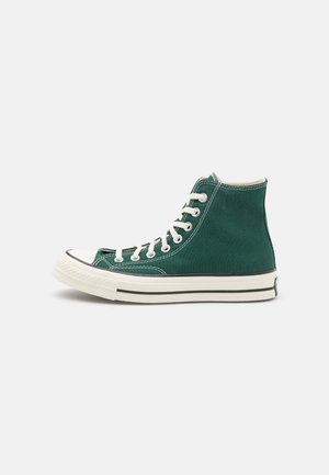 Groene hoge canvas sneaker met witte veters, witte rubberen zool en zwarte streepdetails, zijaanzicht tegen een witte achtergrond.