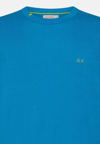 T-shirt in cotone blu con scollatura rotonda, accentuazione gialla vicino al colletto e piccolo logo ricamato in giallo sulla parte sinistra del petto.