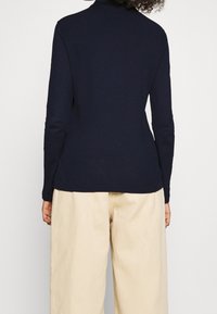 Navy long-sleeve top made of soft material, featuring a round neckline and a fitted design. Paired with beige, loose-fitting pants.