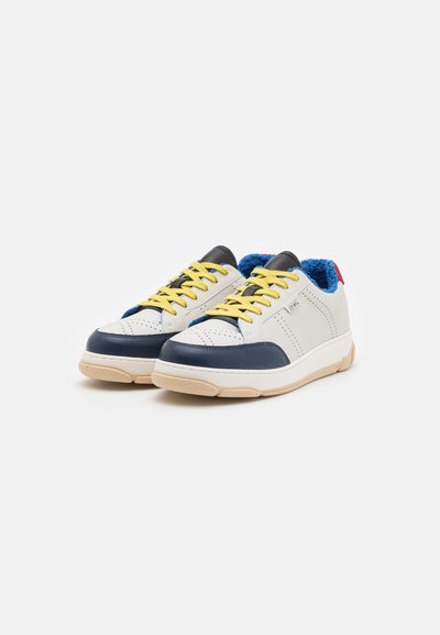 Baskets avec une tige en cuir blanc, des accents bleu marine, des lacets jaunes et une doublure texturée bleue. Semelle en caoutchouc avec une semelle intermédiaire beige.