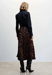 Camisa negra con cuello combinada con una falda de tablas que presenta un patrón abstracto marrón, complementada con botas de tacón alto negras.