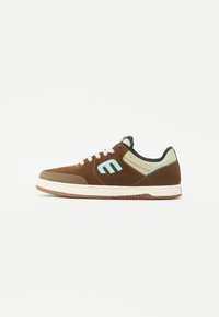 Brun mockasen sneaker med ljusblå detaljer, beige häl och vit mellansula. Har en texturerad sidodel och en brun gummi sula.