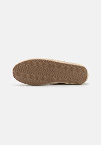 Sole of a shoe with a wave pattern in light brown rubber, featuring a textured edge and a beige, woven-like border for added grip.