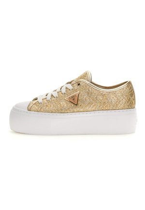 Sneaker à plateforme basse avec texture tissée dorée, lacets blancs et semelle blanche en caoutchouc avec un logo Guess doré triangulaire sur le côté.
