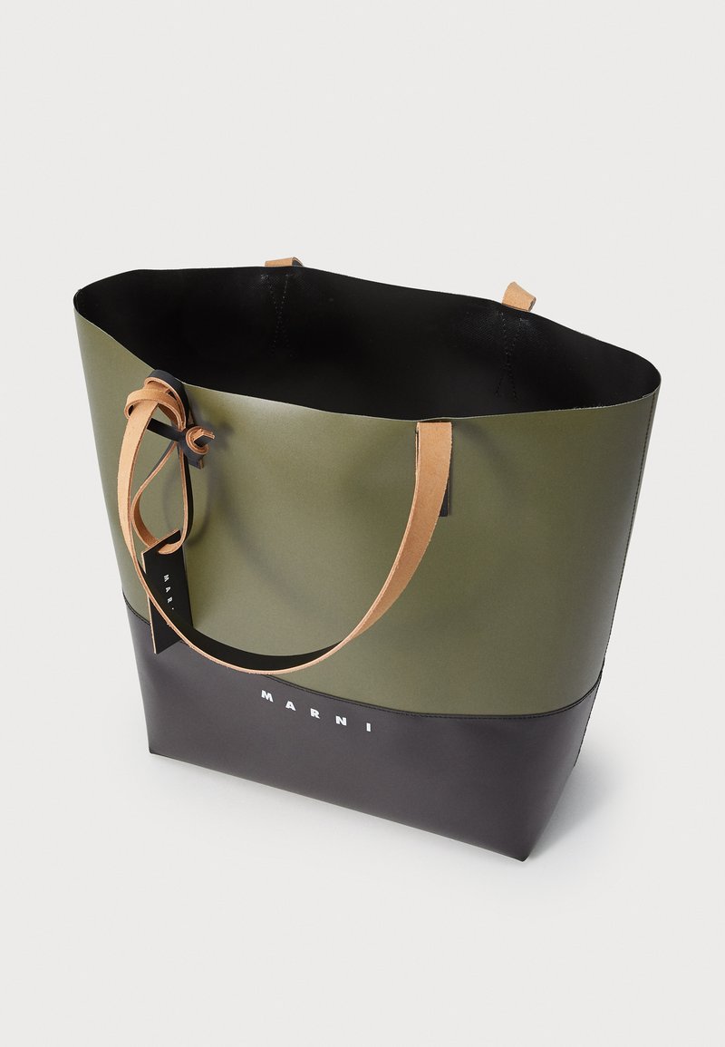 Borsa tote verde e nera con una superficie liscia, dotata di manici in pelle beige e un logo stampato sul davanti. Design senza chiusura superiore.