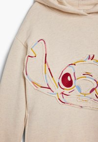 Beige színű kapucnis pulóver, multicolor hímzett Stitch mintával, feltűnő piros szemmel és részletes kék, sárga és rózsaszín varrással.