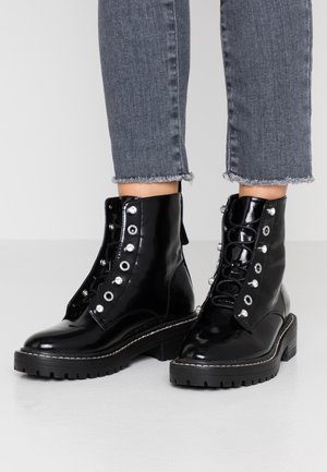 Zwarte patenten leren enkellaarzen met zilveren ooggaten, dikke zwarte zolen en een vetersluiting. Gecombineerd met versleten grijze denim jeans.