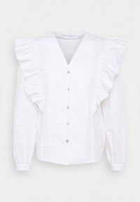 Blouse blanche à manches longues avec boutons sur le devant, épaules volantées, col en V et panneaux verticaux texturés décoratifs à l'avant.