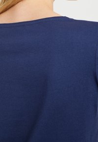 Tmavě modré bavlněné tričko s kulatým výstřihem a krátkými rukávy, hladké na dotek a jednobarevné, zobrazeno z zadního pohledu.