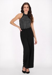 Pantaloni evazați negri cu talie înaltă, asociați cu un top halter din perle negre și argintii. Topul are un model vertical de perle și un design ajustat.