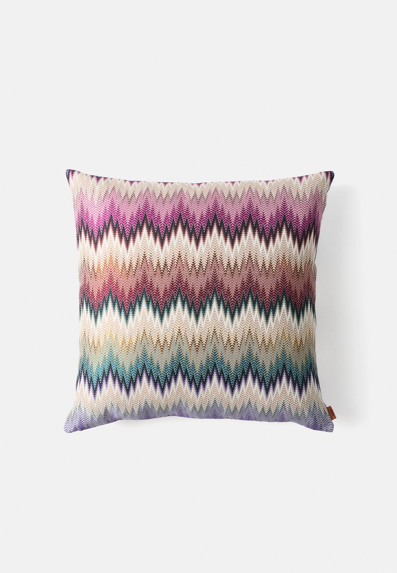 Kvadrātveida spilvens ar zigzaga adījuma rakstu purpura, rozā, bēša, brūnā, tilla un zilā toņos uz baltas fona.