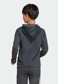 Haut à capuche noir avec un cordon de serrage, présentant une texture douce et des poignets côtelés, porté par un enfant, vu de dos.