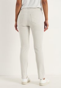 Ljust grå, åtsittande jeans med lätt stretch. Har bakfickor med dekorsömmar och medelhög midja. Kombineras med vita sneakers.