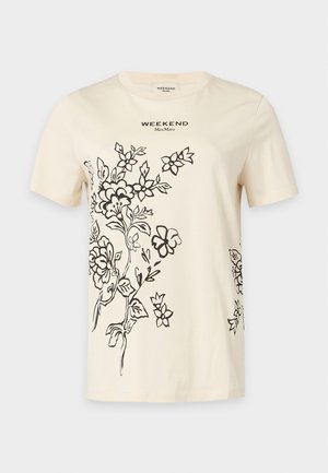 Kobieta ubrana w beżowy t-shirt z czarnym kwiatowym nadrukiem, dwu- tonową plisowaną spódnicę midi w jasnym i ciemnym żółtym kolorze, czarny pasek oraz brązowe botki za kostkę.