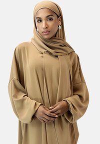 Beige långärmad tunika med löst snitt och matchande hijab. Slät tyg med subtil lyster; har sid sömsdetaljer och oversized ärmar.
