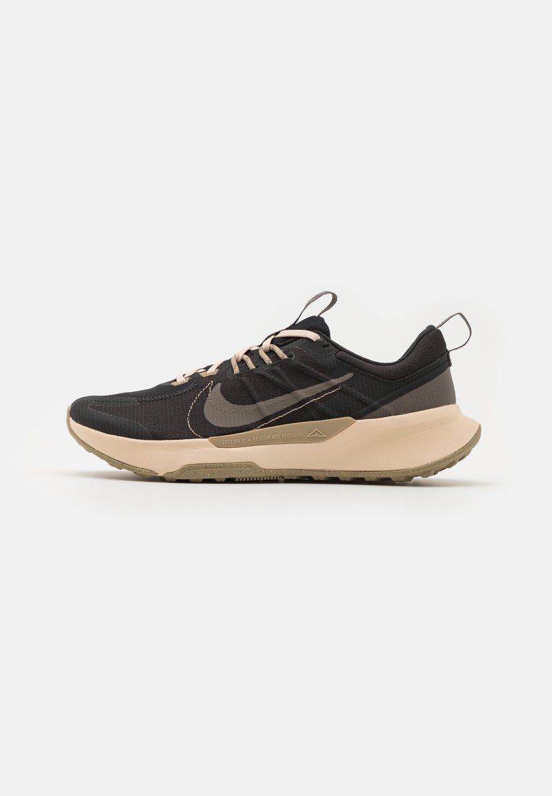 Chaussure de running Nike noire et beige avec fermeture à lacets à l'avant, semelle coussinée et languettes sur la languette et le talon sur fond blanc.