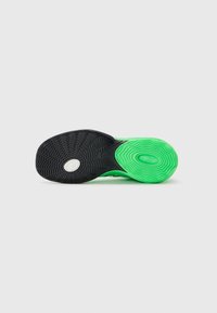 Sål af en sneaker med sort og lys grøn struktureret gummi med greb, der viser et hvidt cirkulært logo nær det sorte grebsområde.