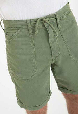 Pantaloncini verdi in cotone con tasche applicate frontali e vita con coulisse, indossati con una camicia bianca, mostrati dalla vita a metà coscia.