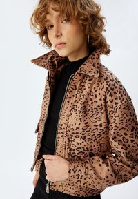 Leopardmönstrad jacka i brunt med svarta fläckar, med blixtlås framtill, hög krage och textilier med struktur. Matchad med en svart topp.