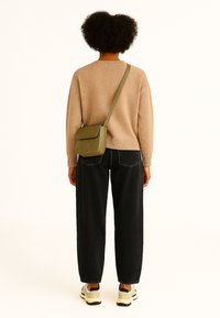 Beige gebreid sweater, zwarte wijde jeans, groene crossbody tas met quilten patroon, en beige sneakers, gezien vanuit de achterkant.