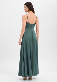 Lange, mouwloze jurk van donkergroene satijn met een vloeiende rok. Heeft dunne bandjes en een verborgen rits aan de achterkant.