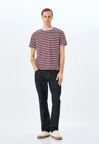 Camiseta de manga corta a rayas en burdeos y blanco, combinada con jeans oscuros. El conjunto se completa con un collar blanco y zapatillas de color claro.