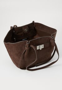 Braune Wildleder-Handtasche mit einem geräumigen Innenraum, einem magnetischen Druckverschluss und einem silberfarbenen Hardware-Akzent auf der Vorderseite. Dünne Schultergurte.