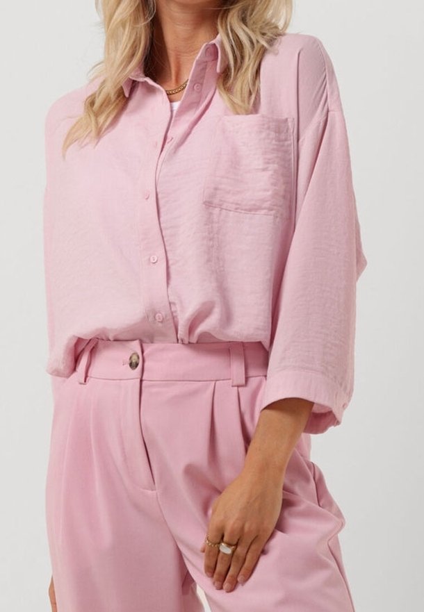 Camicia button-up rosa chiaro con tasca, vestibilità morbida, tessuto strutturato, abbinata a pantaloni a vita alta rosa coordinati.