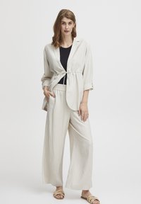 Svijetlosmeđi dvodijelni outfit koji se sastoji od prugaste jakne s remenom i širokim hlačama. Komplet ima mekanu teksturu i opušten kroj.