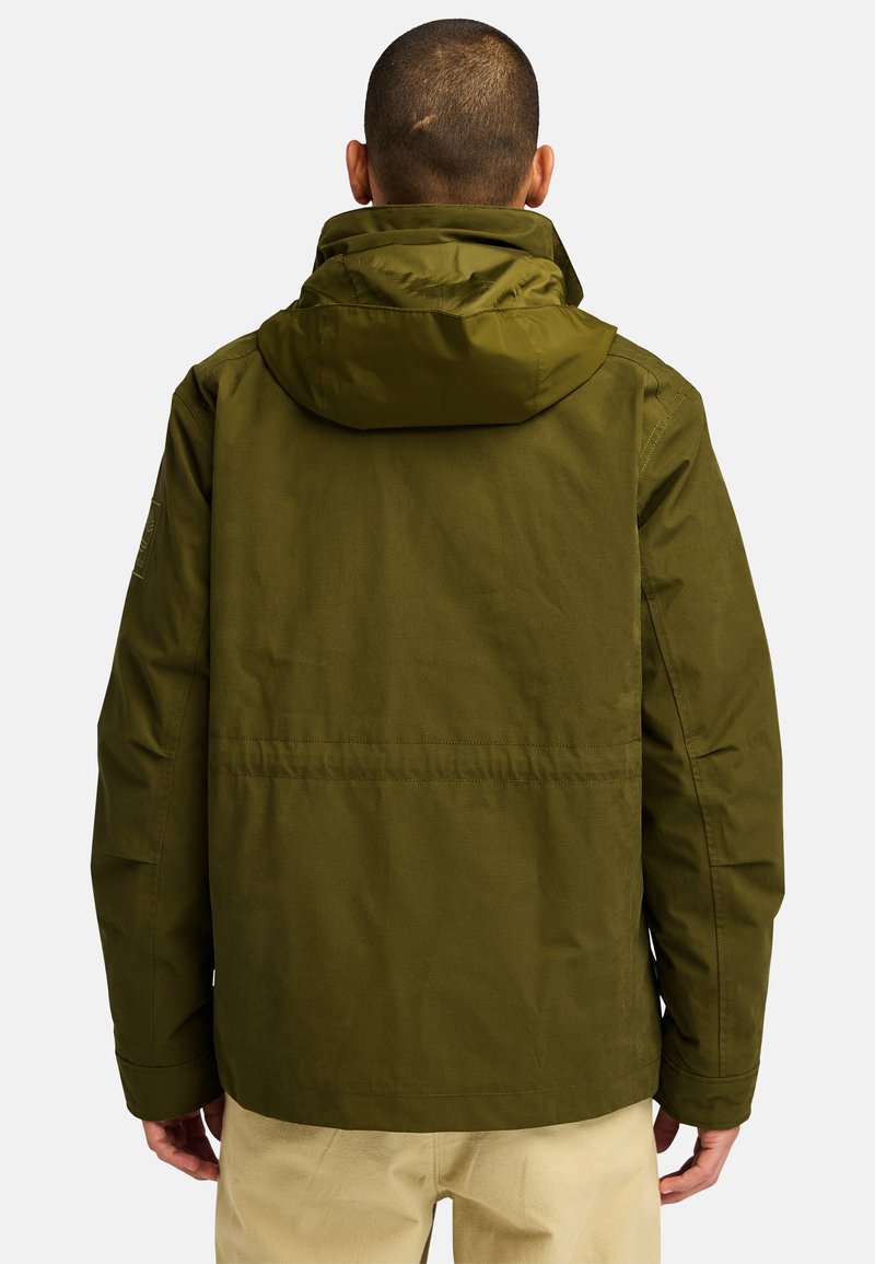 Giacca cappuccio verde oliva con una texture liscia e una vestibilità rilassata. Presenta una cucitura lungo la schiena e una toppa sulla manica.