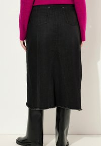 Jupe en denim noir avec un ourlet effiloché, des poches arrière et une couture centrale au dos. Assortie à des bottes noires montant jusqu'aux genoux.