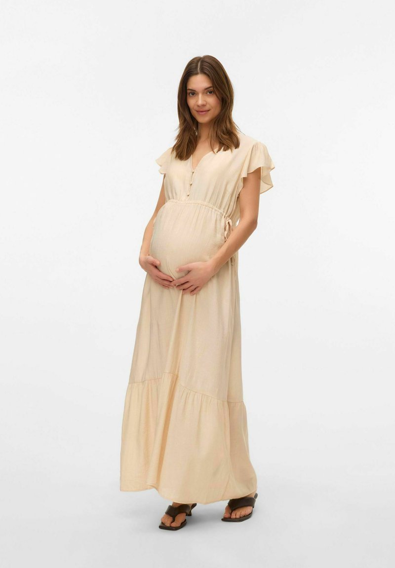 Beige äitiysmekko, jossa on lyhyet liehuvat hihat, V-pääntie, napit ja kootut vyötärö, jossa on kerroksellinen hame ja virtaava kangas.