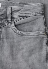 Gros plan sur un jean denim gris montrant la poche avant, la passants de ceinture et les détails de couture.