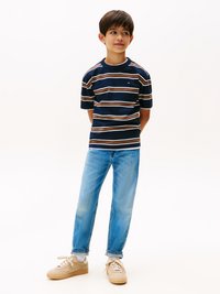 Tricou cu dungi bleumarin, cu dungi maronii și crem, asortat cu blugi bleui deschis și adidași bej cu șireturi albe. Textură a țesăturii netedă.