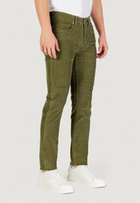 Pantaloni verde olive con una finitura testurizzata, dotati di una vestibilità slim, tasche frontali e chiusura con bottone metallico, abbinati a sneakers bianche.