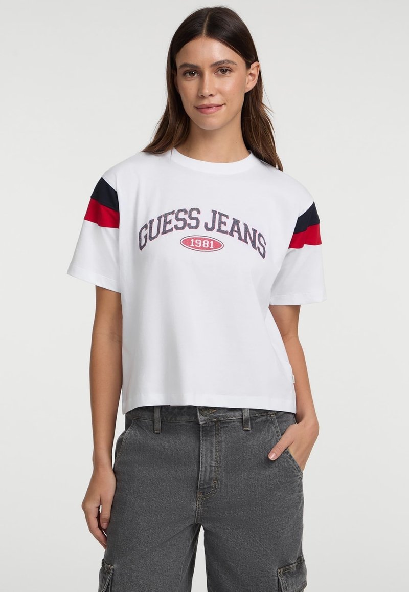 Biele skrátené tričko s logom "GUESS JEANS 1981" v tmavo červenej farbe, s námornícko modrými a červenými pruhmi na rukávoch. Mäkká textúra látky.