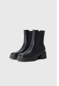 Botas de cuero negras hasta el tobillo con puntera redondeada, paneles laterales elásticos y tacón cuadrado. Textura lisa, diseño minimalista y suela resistente.