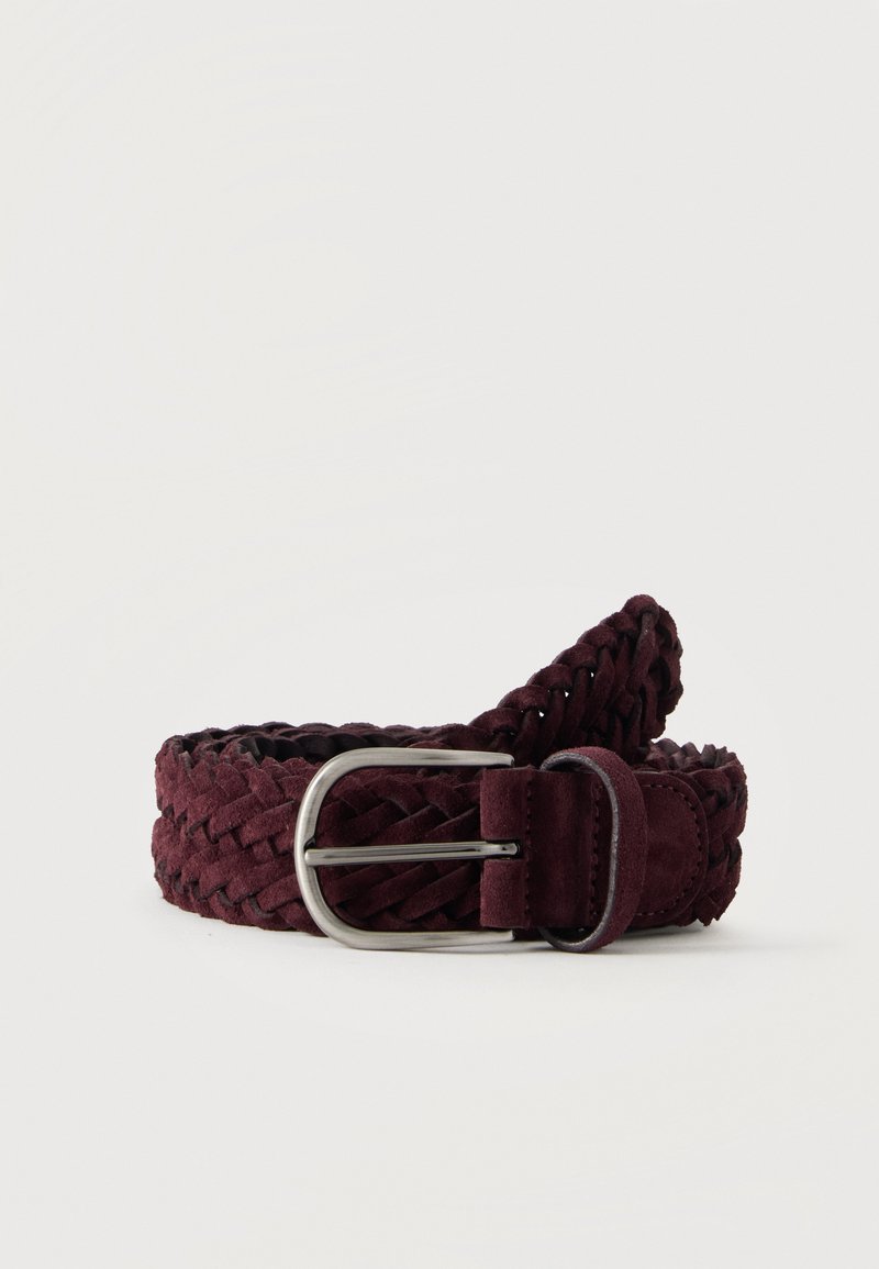 Ceinture en daim bordeaux foncé tressée avec boucle métallique argentée roulée sur fond blanc.