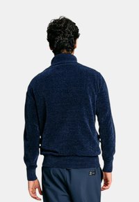 Maglione pullover blu navy con colletto alto, tessuto testurizzato, polsini e orlo a costine, e una vestibilità comoda. Presenta un'etichetta sul lato.