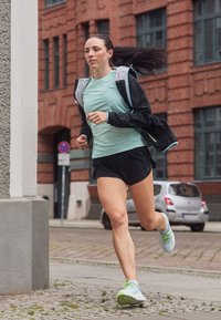Miętowozielony top sportowy, czarne szorty, czarna kurtka z jasnoniebieskimi akcentami oraz wielokolorowe buty biegowe na kocim łbie.