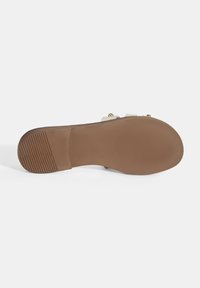 Bruine rubberen zool met horizontale groeven, voorzien van een gladde tan-kleurige zone, contrasterende beige bandjes en gouden hardware accenten.