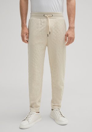 Beige sweatpants met een gestructureerd gewatteerd patroon, elastische tailleband en koord; gecombineerd met witte sneakers.