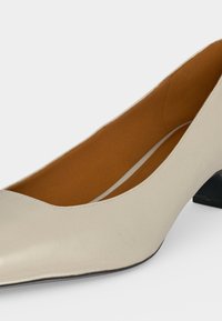 Chaussure beige pour femme à talon bas avec bout pointu et doublure intérieure marron, vue en gros plan sur fond blanc.